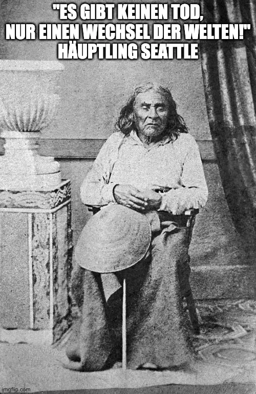 Historische Schwarzweißfotografie eines älteren Mannes mit langem Haar, der mit einem Hut auf dem Schoß auf einem Stuhl sitzt. Darüber der Text: „Es gibt keinen Tod, nur einen Wechsel der Welten!“ Häuptling Seattle.