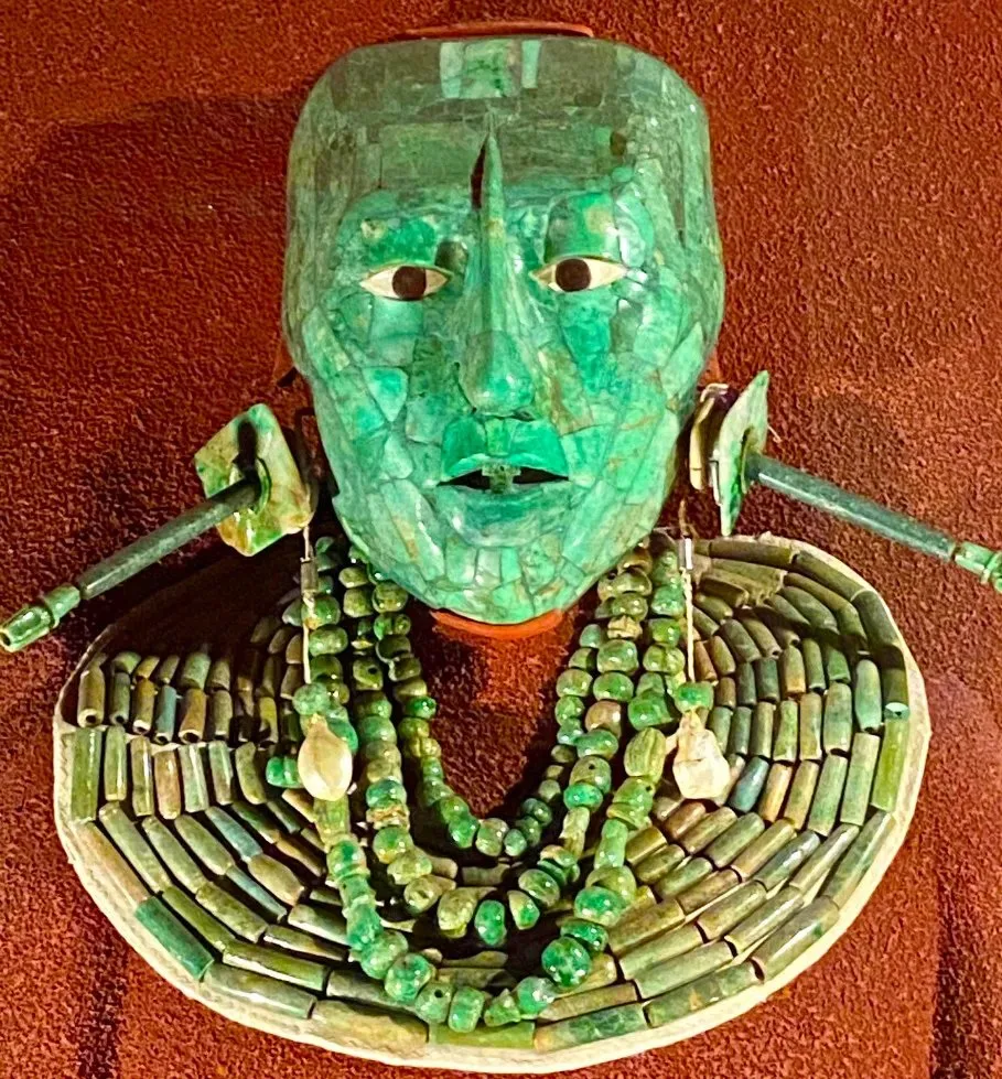 A jade mosaic funerary mask with inlaid white and dark eyes, displayed with jade ear ornaments, strands of jade beads and a broad beaded collar.