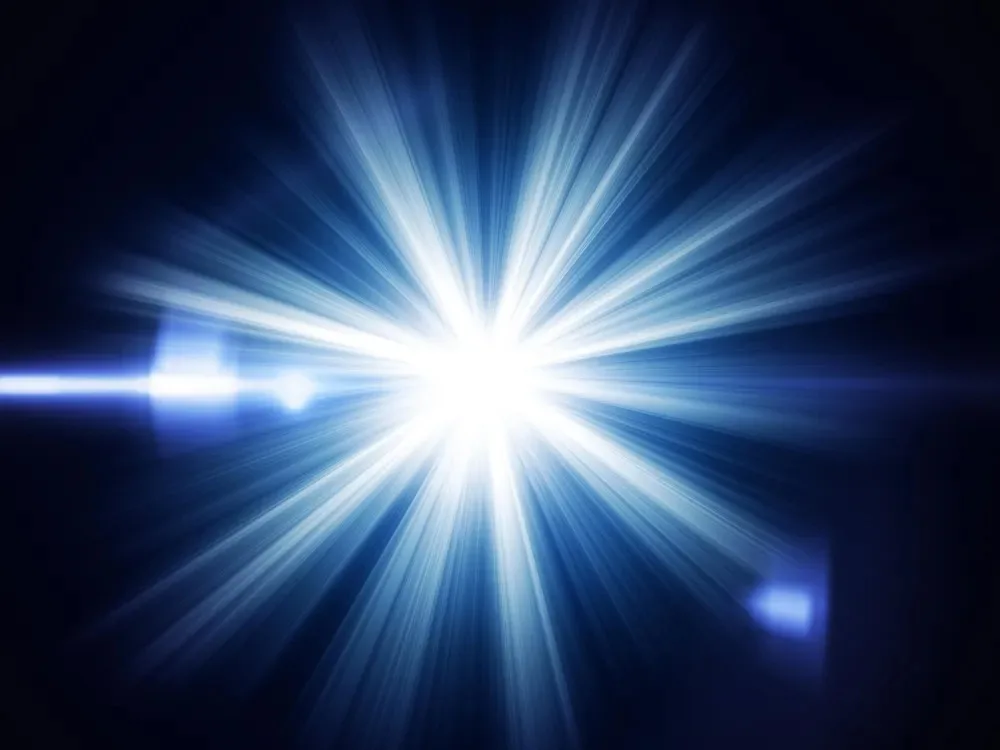 A brilliant white starburst radiating beams of blue light against a dark background, with a streak of lens flare to one side.