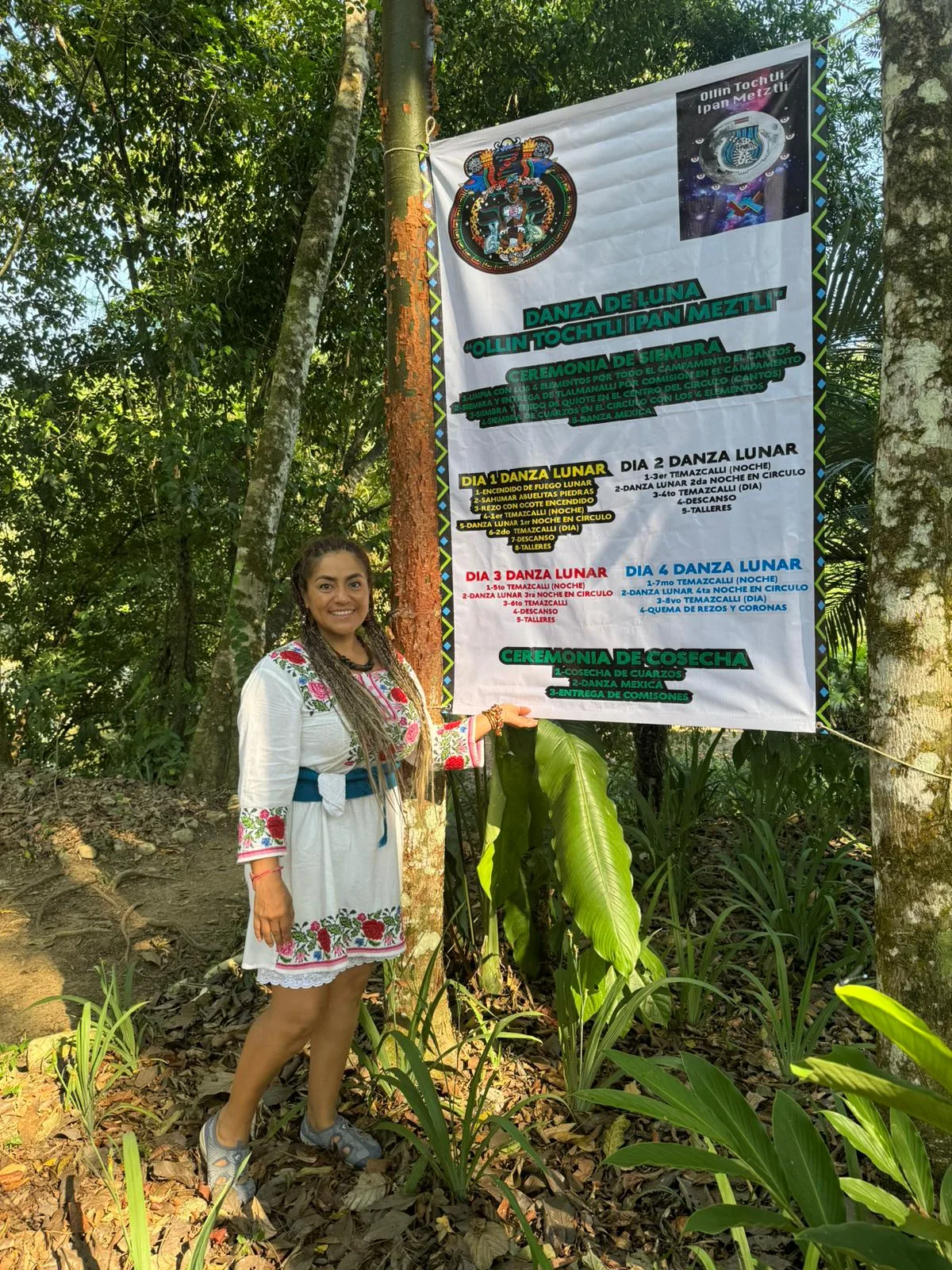 A smiling woman in an embroidered white dress stands in the jungle beside a banner announcing the Moon Dance "Ollin Tochtli Ipan Meztli" and its schedule of ceremonies.
