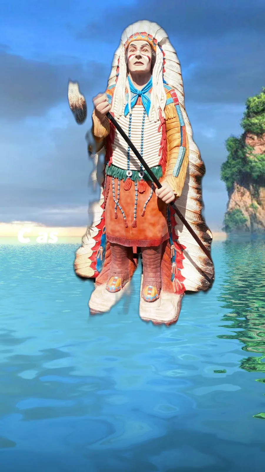 A carved and painted statue of a chief in a long feathered headdress, holding a feathered staff, edited to appear standing on turquoise water beneath a cloudy sky.