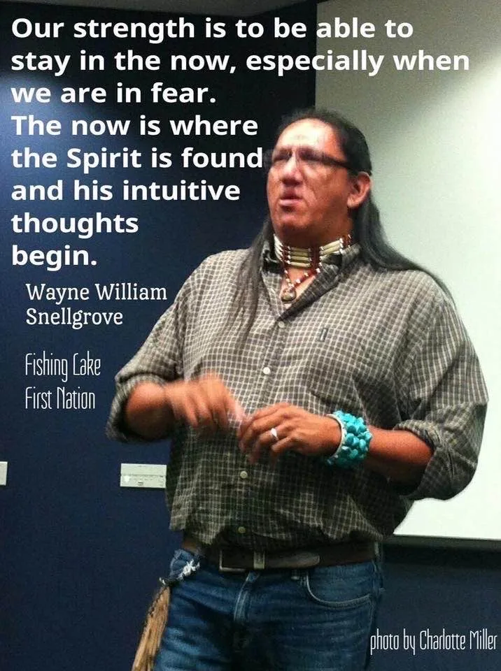 Wayne William Snellgrove of Fishing Lake First Nation, with long dark hair, a bone choker and turquoise cuff, speaks in a room. Overlaid quote: our strength is staying in the now, especially in fear, where Spirit is found.