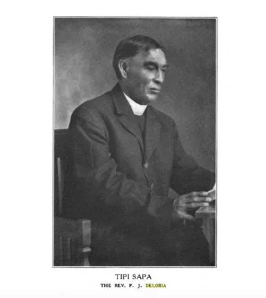 Black-and-white portrait of Tipi Sapa, Rev. Philip J. Deloria, in a clerical collar and dark suit, seated at a desk with a book, captioned with his name.