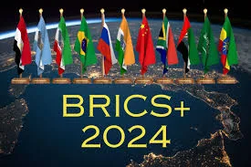 A row of national flags, including those of Brazil, Russia, China and South Africa, stands above a night view of Earth from space, with the words "BRICS+ 2024" in gold.