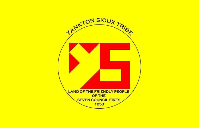 Yellow flag of the Yankton Sioux Tribe with a circular seal holding a red geometric emblem and the words "Land of the Friendly People of the Seven Council Fires, 1858."
