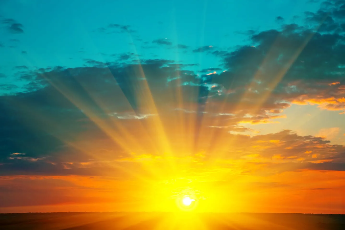 A brilliant golden sun rising over a flat horizon, its rays streaming upward through dark clouds into a turquoise sky.