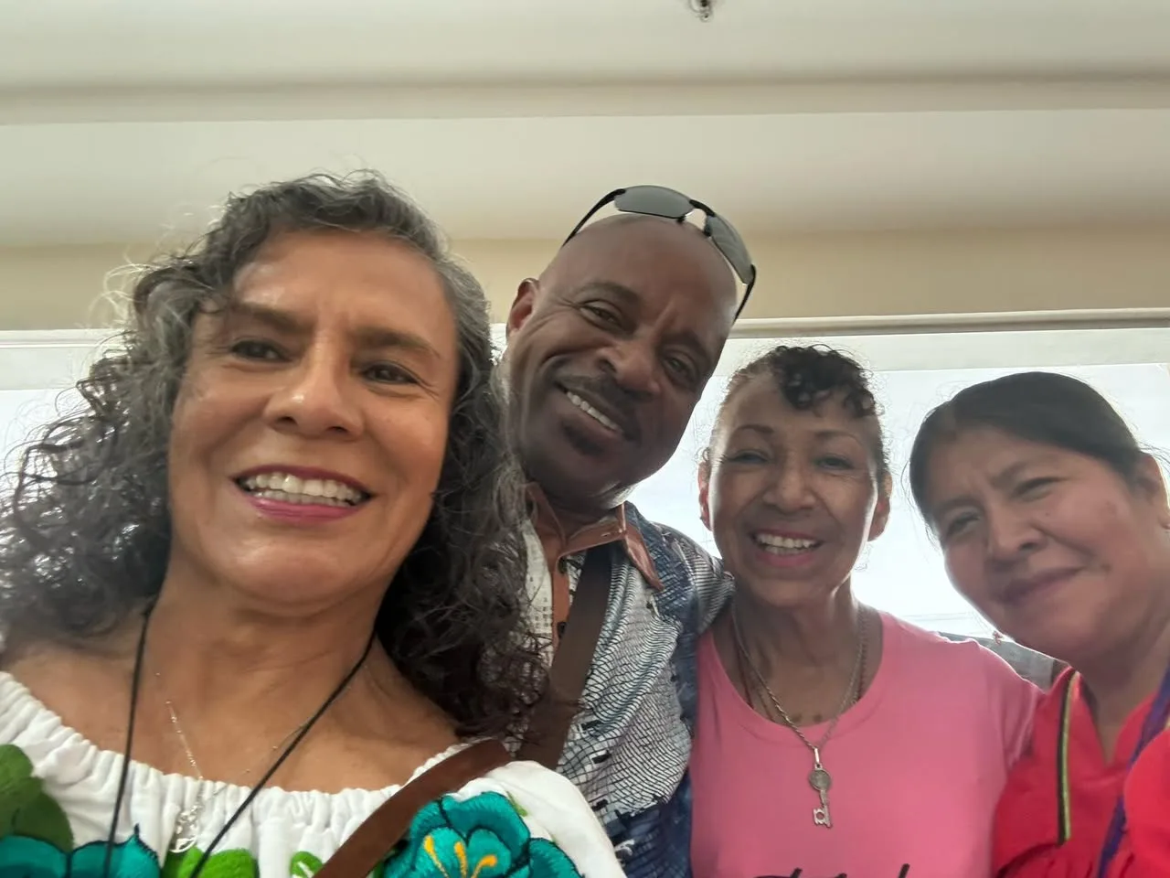 A smiling selfie of four people, three women and a man, posing close together indoors.